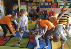 Dzieci stoją na dywanie i podają sobie dynie.