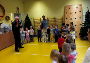Dzieci stoją w pólkolu i słuchają dźwięków instrumentów.