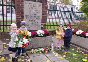 Dzieci składają kwiaty i znicze przy miejscu pamięci narodowej.