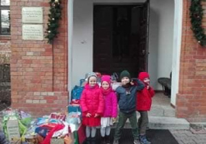 Dzieci stoją pod domem Seniora z przygotowanymi prezentami.