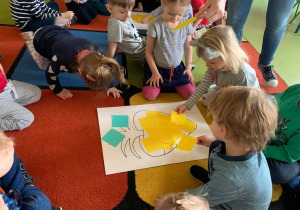 Dzieci układają z kolorowych kartoników kształt marchewki.
