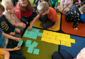 Dzieci układają z kolorowych kartoników kształt marchewki.