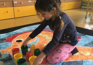 Dziewczynka układa kolorowe kubki według kodu.
