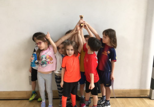 Dzieci trzymają w rękach statuetkę, wygraną w zawodach sportowych.
