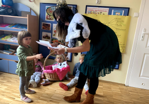 Nauczycielka przebrana za czarownicę wręcza dziewczynce nagrodę za konkurs halloweenowy.