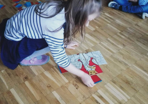Dziewczynka układa puzzle z obrazkiem orła białego.