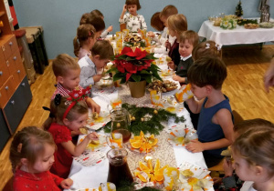 Dzieci siedzą przy wigilijnym stole i jedzą tradycyjne potrawy.