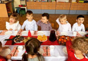Dzieci siedzą przy wigilijnym stole i jedzą tradycyjne potrawy.