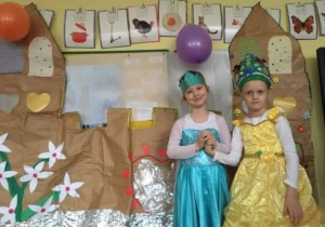Dziewczynki przebrane za księżniczki stoją na tle papierowego zamku.