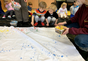 Dzieci malują płotno farbami.