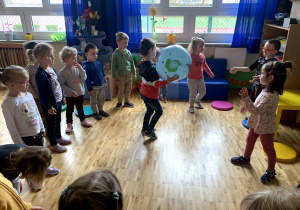 Dzieci podają sobie piłkę z wzorem globusa.