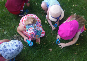 Dzieci oglądają trawę przez lupy.
