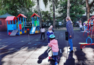 Dzieci jeżdżą na hulajnogach na przedszkolnych placu zabaw.