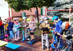 Dzieci jeżdżą na hulajnogach na przedszkolnym placu zabaw.