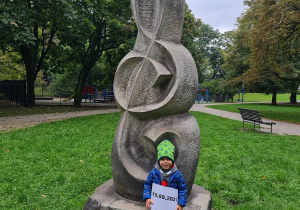 Dziecko siedzi przy pomniku przedstawiającym klucz wiolinowy.