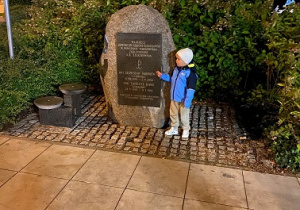 Dziecko stoi przy pomniku pamięci Powstania Warszawskiego.