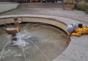 Dziecko moczy dłoń w fontannie ze Złotą Kaczką.