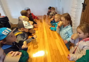 Dzieci siedzą przy długim stole. Piją lawendową lemoniadę i jedzą lawendowe ciastka.