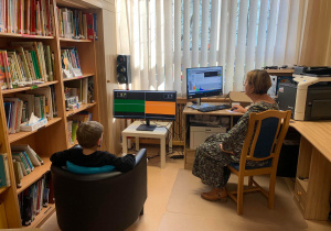 Dziecko siedzi przed ekranem komputera podczas terapii Biofeedback. Po prawej stronie siedzi terapeuta przed swoim ekranem z danymi terapii.