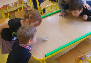 Dzieci w parach przedmuchują piłeczkę ping pongową na drugą stronę stołu.