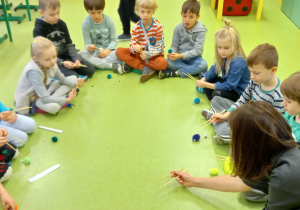 Nasze hobby. Dzieci siedzą w kole na podłodze i uczą się, jak posługiwać się pałeczkami.