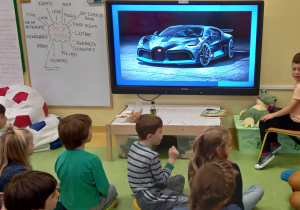 Nasze hobby. Chłopiec pokazuje nowoczesne auta na dużym ekranie.