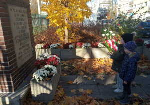 Święto Odzyskania Niepodległości. Dwoje dzieci składa kwiaty w miejscu pamięci narodowej.