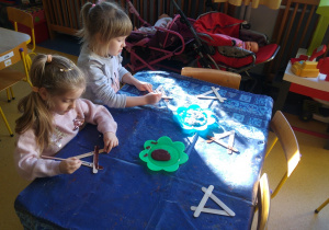 Dzieci malują renifery z patyczków na choinkę.