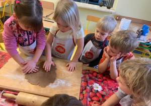Dzieci wałkują ciasto na pierniczki.