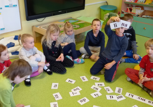 Dzieci na podłodze siedzą wokół kartek z sylabami oraz układają z nich wyrazy.