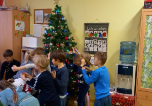 Dzieci ubierają choinkę w sali przedszkolnej.