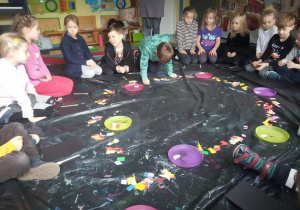 Warsztaty Szkatułka. Dzieci siedzą na czarnej folii i układają kolorowe karteczki.
