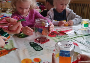 Dzieci wyklejają słoiki kolorowymi tasiemkami.