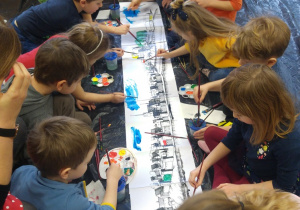 Dzieci wspólnie malują duży pejzaż.
