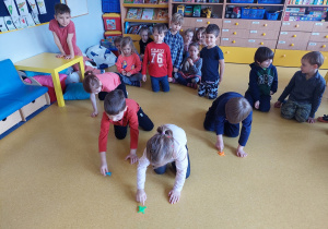 Dzieci ścigają się skaczącymi żabkami po podłodze.