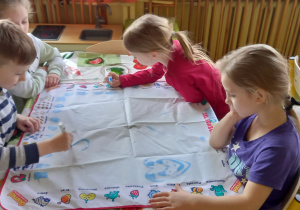 Projekt woda. Dzieci siedzą przy stole i piszą oraz malują wodą na specjalnej macie.