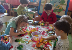 Dzieci wykonują wielkanocne ozdoby na kiermasz wielkanocny z kolorowych piórek.