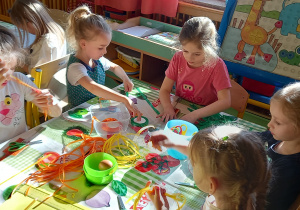 Dzieci wykonują wielkanocne ozdoby na kiermasz wielkanocny z kolorowych wstążek.