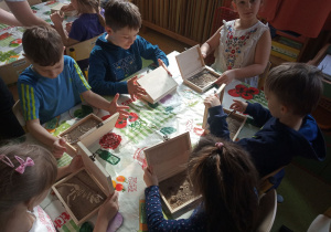 Warsztaty o dinozaurach. Dzieci siedzą przy stole nad pudełkami ze skamieniałymi kośćmi dinozaurów.