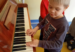 Chłopiec próbuje grać na pianinie.