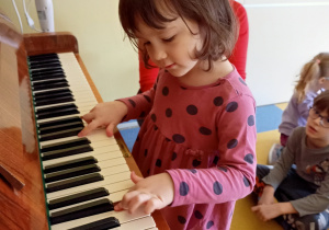 Dziewczynka próbuje grać na pianinie.