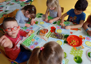 Dzieci wyklejają wiosenne obrazki plasteliną.