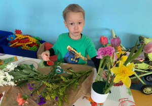 Chłopiec komponuje bukiet z kwiatów.