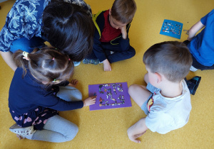 Dzieci układają na kartce labirynty z kamyczków.