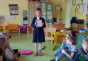 Dziewczynka pokazuje kolegom ulubioną książkę w sali przedszkolnej.