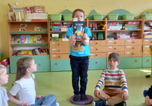 Dziewczynka pokazuje kolegom ulubioną książkę w sali przedszkolnej.
