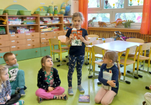 Dziewczynka pokazuje kolegom ulubioną książkę w sali przedszkolnej.