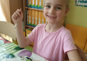 Dziewczynka maluje figurkę gipsową w kształcie kwiatków.