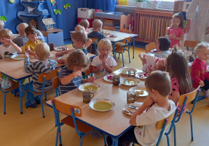 Dzieci siedzą przy stołach i jedzą.