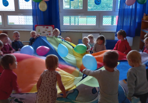 Dzień Przedszkolaka - dzieci bawią się dużą kolorową chustą i balonami.